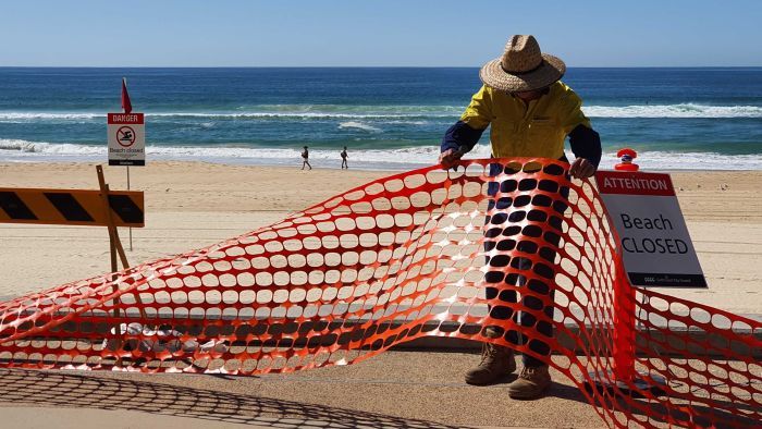 A council worker removes barriers installed at Surfers Paradise on the Gold Coast. However the State's border restrictions remain in place, despite industry pleas. Photo: ABC