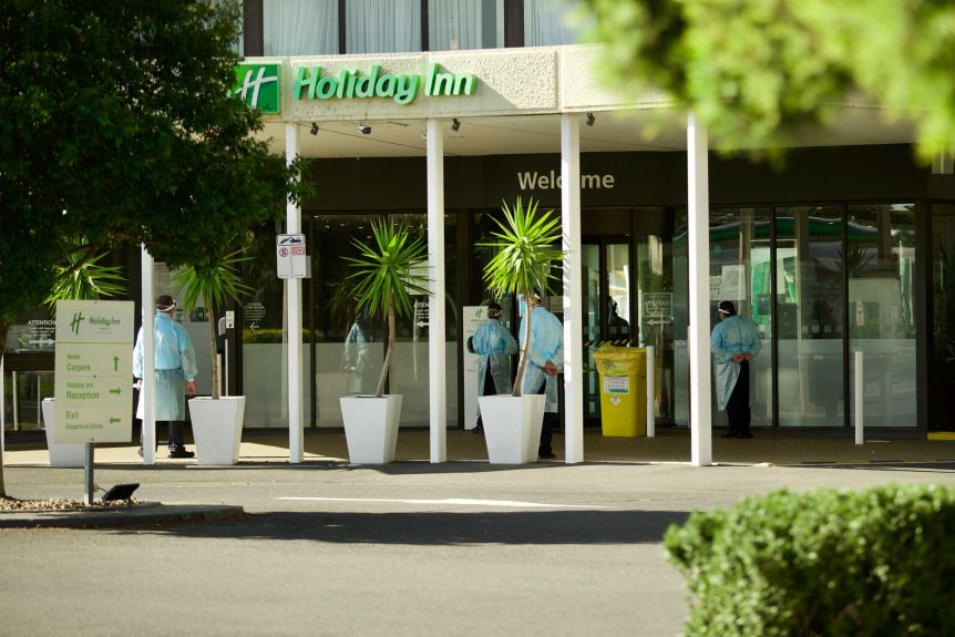 Staff in personal protective equipment as returned travellers are moved from the Holiday Inn Melbourne yesterday. Photo: ABC News
