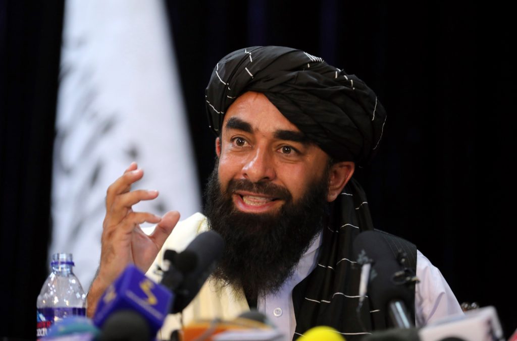 In front of a Taliban flag, Taliban spokesman Zabihullah Mujahid speaks at at his first news conference, in Kabul, Afghanistan, Tuesday. Mujahid vowed that the Taliban would respect women's rights, forgive those who resisted them and ensure a secure Afghanistan as part of a publicity blitz. (AP Photo/Rahmat Gul)