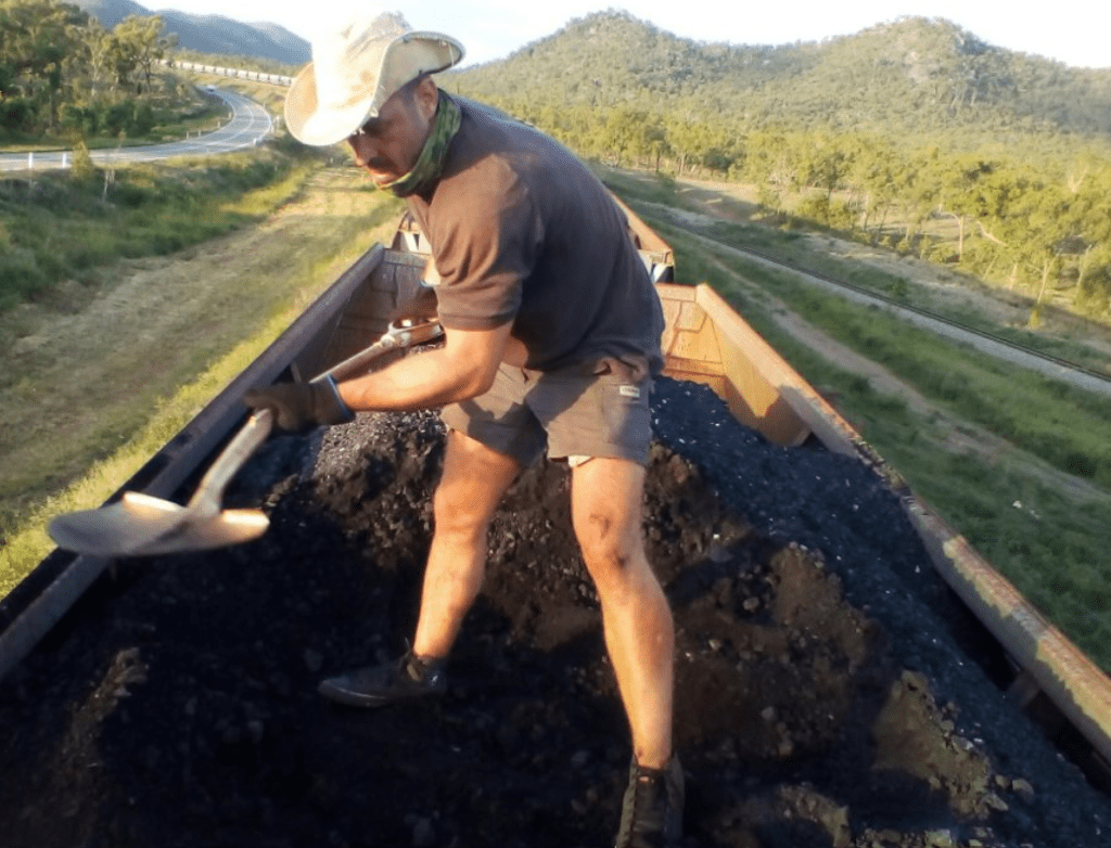 Activist Kyle Magee shovelling coal from an Adani train (courtesy Frontline Action on Coal)