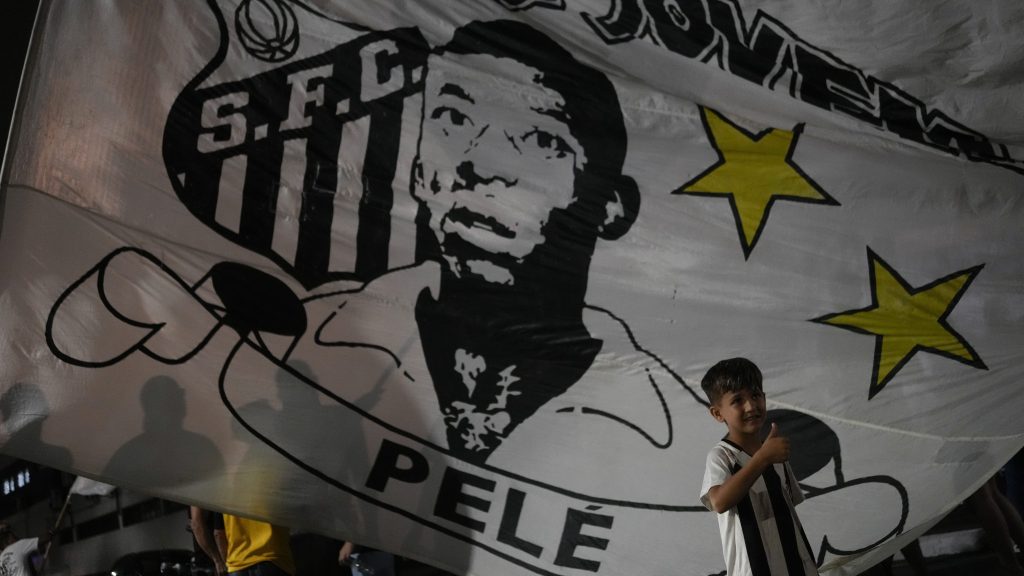 A boy poses in front of a flag of the late Brazilian soccer star Pele outside the Vila Belmiro stadium, home of the Santos FC soccer club, in Santos, Brazil. (AP Photo/Matias Delacroix)