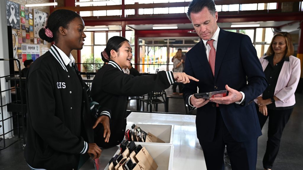 New South Wales Premier Chris Minns learns how to check a phone in during a visit to Condell Park High School. All parents affected will be offered tutoring - over the phone. (AAP Image/Steven Saphore) 