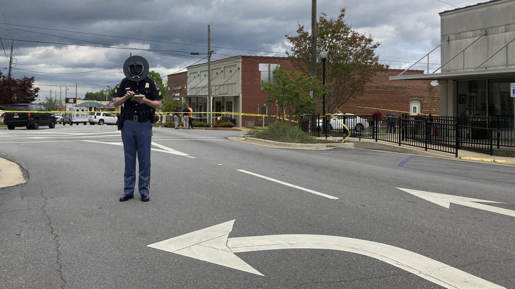 An Alabama state trooper checks his phone as investigators work at the site of a fatal shooting in downtown Dadeville, Ala., on Sunday, April 16, 2023. Several were killed during a shooting at a birthday party Saturday night, the Alabama Law Enforcement Agency said. (AP Photo/Jeff Amy)