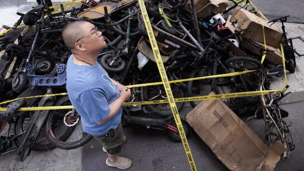 A man stands near a pile of burned e-bikes at the site of an overnight fire at an e-bike store that killed four people in the above apartment building in the Chinatown neighborhood of New York,  EPA/JUSTIN LANE