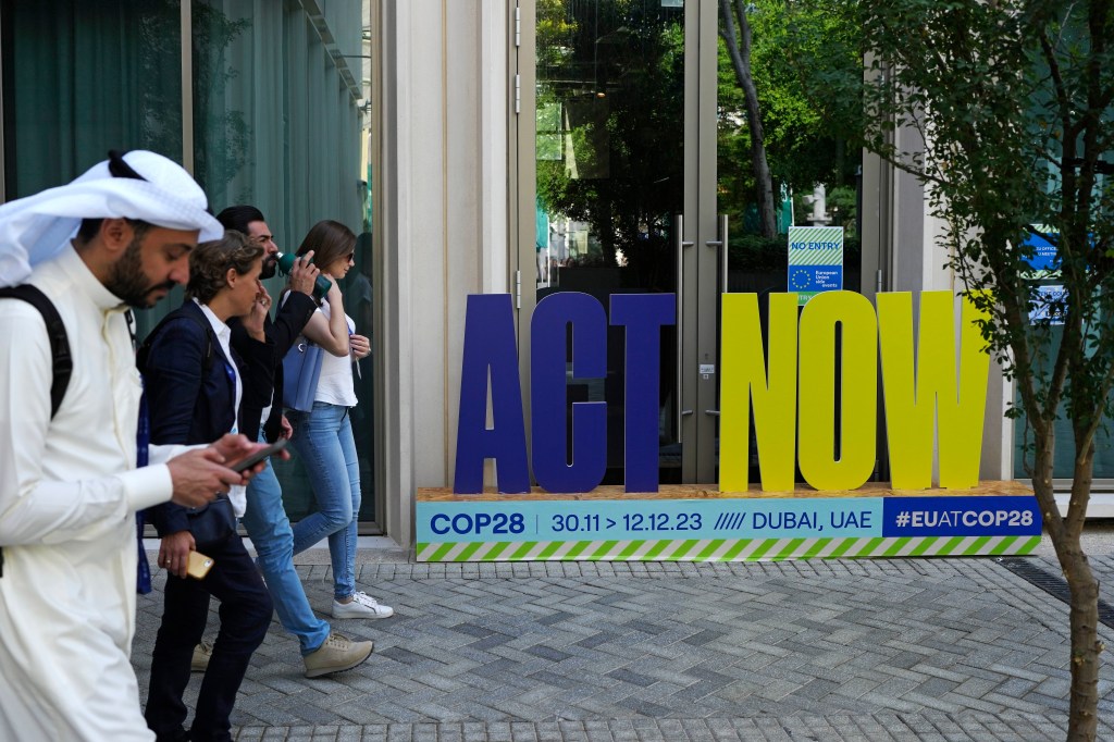 A group walks near a sign that reads "act now" at the COP28 U.N. Climate Summit in Dubai, United Arab Emirates. (AP Photo/Rafiq Maqbool)