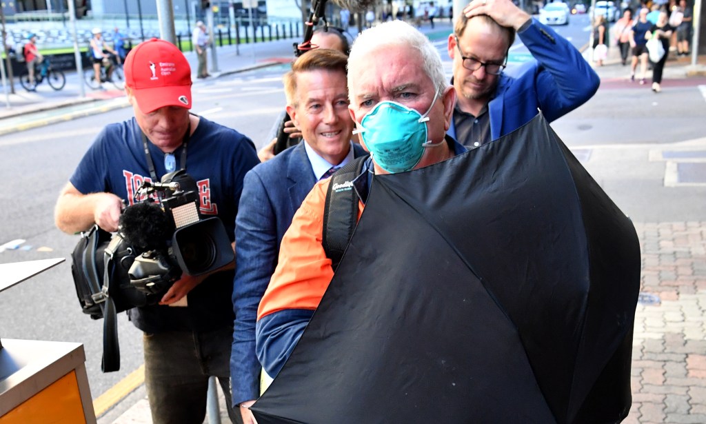 Ian Seeley, who is the stepson of main suspect Raymond Peter Mulvihill, is seen trying to shield himself from the media as he leaves the Brisbane Coroners Court in Brisbane, Wednesday, March 24, 2021.. (AAP Image/Darren England) 
