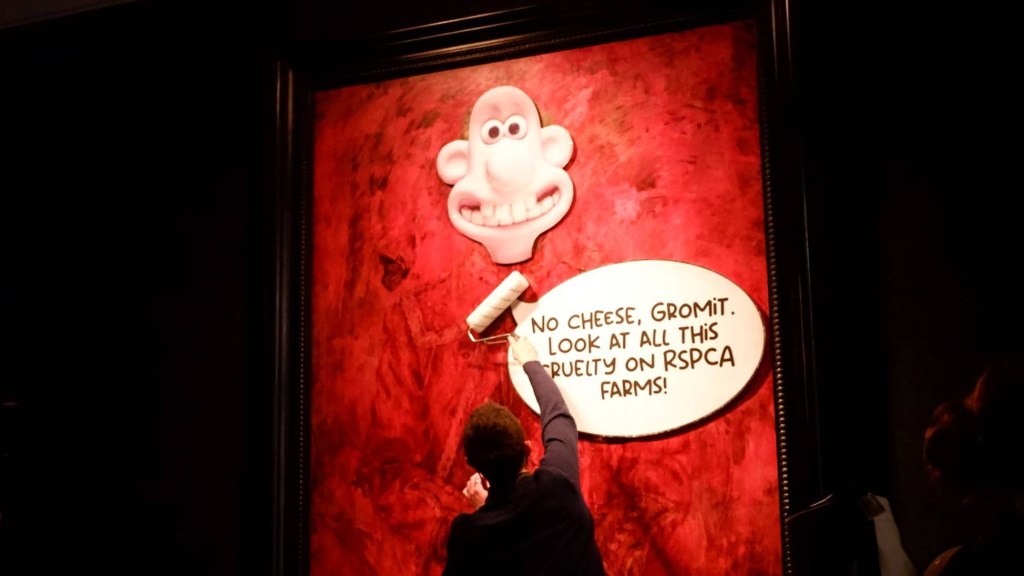 A handout photo made available by animal rights group Animal Rising shows an activist affixing posters onto the painting of King Charles III at Philip Mould gallery.